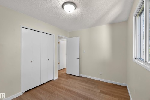 Wood-finish flooring, white bi-fold closet doors, white walls, flush mount ceiling light, and a window with white trim - 14725 43A Avenue Nw, Edmonton, AB - Indoor Photo Showing Other Room