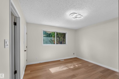 Wood-finish flooring with neutral wall tones, a modern flush-mount ceiling light, and a window providing natural illumination - 14725 43A Avenue Nw, Edmonton, AB - Indoor Photo Showing Other Room