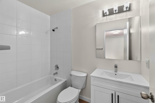 Bathroom featuring a white subway tile shower surround, a white vanity with integrated sink, a rectangular vanity mirror, and a chrome light fixture - 14725 43A Avenue Nw, Edmonton, AB - Indoor Photo Showing Bathroom