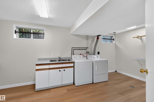 Laundry area featuring a utility sink, white cabinetry, and wood-finish flooring - 14725 43A Avenue Nw, Edmonton, AB - Indoor Photo Showing Laundry Room