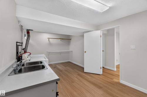 Utility room featuring wood-finish flooring, a double basin stainless steel sink, countertop, and built-in shelving - 14725 43A Avenue Nw, Edmonton, AB - Indoor Photo Showing Kitchen With Double Sink