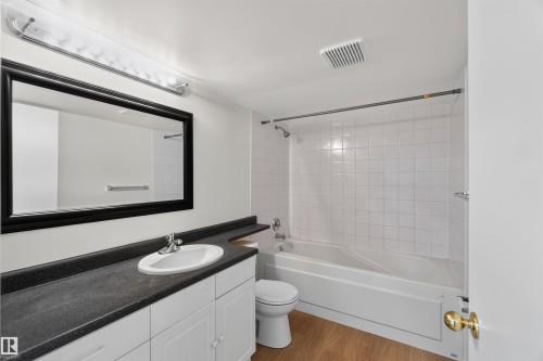 White vanity with dark countertop, large framed mirror, and integrated bathtub with white tile surround - 14725 43A Avenue Nw, Edmonton, AB - Indoor Photo Showing Bathroom