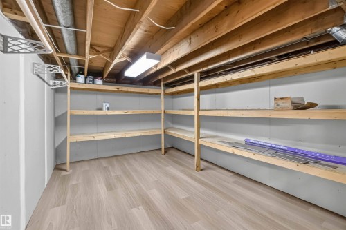 Spacious storage area featuring wood-finish flooring, built-in wooden shelving, and overhead fluorescent lighting - 14725 43A Avenue Nw, Edmonton, AB - Indoor Photo Showing Basement