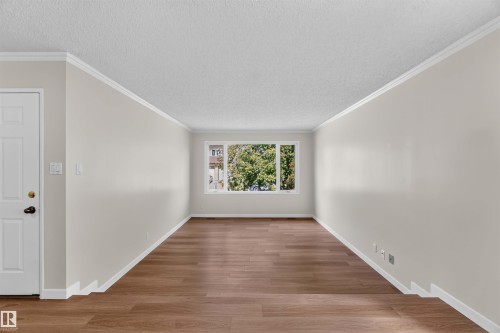 Wood-finish flooring, white baseboards, crown molding, and a paneled entry door - 14725 43A Avenue Nw, Edmonton, AB - Indoor Photo Showing Other Room