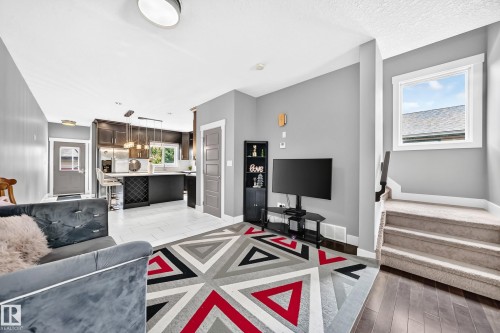 Open-concept living area featuring wood-finish flooring, a contemporary kitchen with dark cabinetry, an island with built-in wine storage, and a carpeted staircase - 12730 118 Street Nw, Edmonton, AB - Indoor Photo Showing Living Room