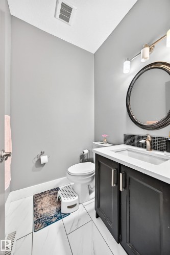 Vanity with integrated sink, black cabinetry, and a circular mirror - 12730 118 Street Nw, Edmonton, AB - Indoor Photo Showing Bathroom