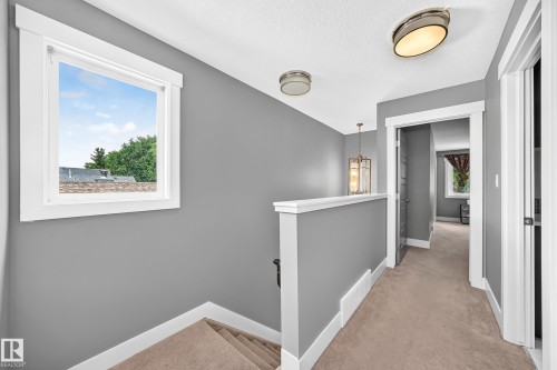 Carpeted hallway featuring a window with white trim, a built-in half-wall, and overhead flush-mount lighting - 12730 118 Street Nw, Edmonton, AB - Indoor Photo Showing Other Room