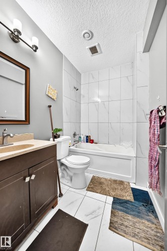 Bathroom featuring white tiled flooring, a bathtub with white tiled surround, a dark wood-finish vanity with a single basin, and a framed mirror - 12730 118 Street Nw, Edmonton, AB - Indoor Photo Showing Bathroom