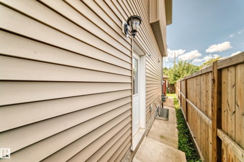 Neutral-toned siding exterior with a white door, an exterior wall-mounted light fixture, and a wood fence - 12730 118 Street Nw, Edmonton, AB - Outdoor