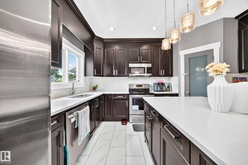 Kitchen featuring dark wood cabinetry, white countertops, tile flooring, stainless steel appliances, and pendant lighting - 12730 118 Street Nw, Edmonton, AB - Indoor Photo Showing Kitchen With Upgraded Kitchen
