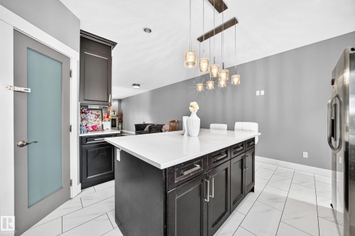 Kitchen island with a light-toned countertop, dark-finish cabinetry, and contemporary pendant lighting - 12730 118 Street Nw, Edmonton, AB - Indoor