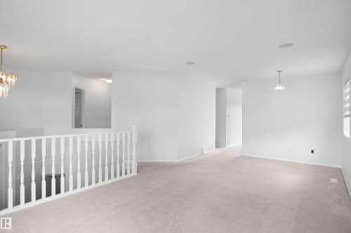Spacious room featuring light-toned carpeting, white painted walls, white spindle railing, and a modern chandelier - 907 Jordan Crescent Nw, Edmonton, AB - Indoor Photo Showing Other Room