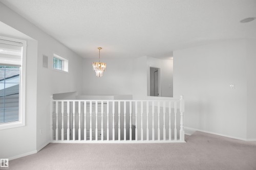 Upper-level space featuring a contemporary chandelier, white window frames, and carpeting - 907 Jordan Crescent Nw, Edmonton, AB - Indoor Photo Showing Other Room