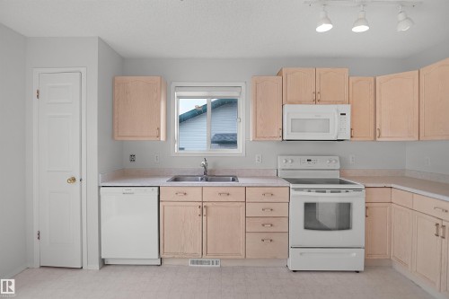Kitchen featuring wood-finish cabinetry, light-toned countertops, stainless steel sink, white dishwasher, and white electric range - 907 Jordan Crescent Nw, Edmonton, AB - Indoor Photo Showing Kitchen With Double Sink
