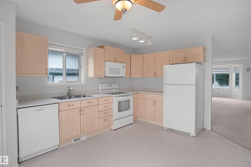 U-shaped kitchen with light wood-finish cabinetry, a double basin stainless steel sink, and a full suite of white appliances - 907 Jordan Crescent Nw, Edmonton, AB - Indoor Photo Showing Kitchen With Double Sink