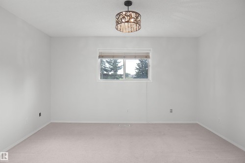 Neutral wall paint, window with blinds, carpeted flooring, and a decorative ceiling light fixture - 907 Jordan Crescent Nw, Edmonton, AB - Indoor Photo Showing Other Room