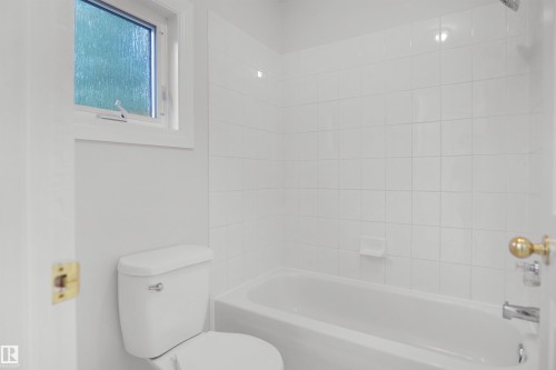 White tile tub surround, white porcelain bathtub, and an integrated white toilet - 907 Jordan Crescent Nw, Edmonton, AB - Indoor Photo Showing Bathroom