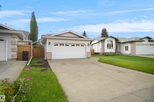 Attached two-car garage with arched window detailing, light-toned siding, stone-finish accents, and a concrete driveway - 907 Jordan Crescent Nw, Edmonton, AB - Outdoor With Facade