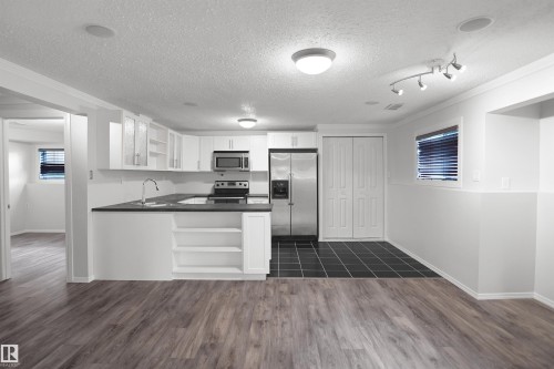 Contemporary kitchen featuring white cabinetry, stainless steel appliances, dark countertops, and tile flooring - 907 Jordan Crescent Nw, Edmonton, AB - Indoor Photo Showing Kitchen