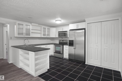 White cabinetry, stainless steel appliances, black square floor tiling, built-in shelving, and bifold closet doors - 907 Jordan Crescent Nw, Edmonton, AB - Indoor Photo Showing Kitchen