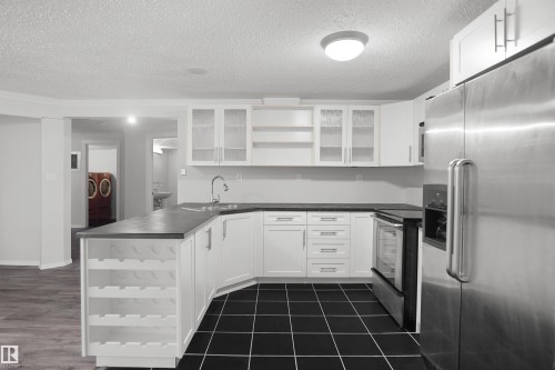 Contemporary kitchen featuring white cabinetry, dark countertops, black tile flooring, and integrated stainless steel appliances - 907 Jordan Crescent Nw, Edmonton, AB - Indoor Photo Showing Kitchen With Upgraded Kitchen
