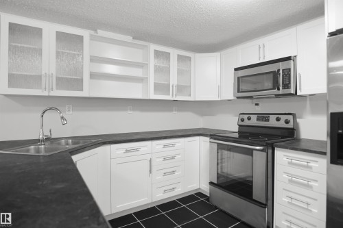 White cabinetry, black countertops, stainless steel appliances, dual basin sink, and black square tile flooring - 907 Jordan Crescent Nw, Edmonton, AB - Indoor Photo Showing Kitchen With Double Sink