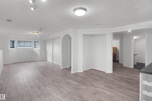 Spacious room featuring wood-finish flooring, multiple windows with blinds, track lighting, and an arched entryway - 907 Jordan Crescent Nw, Edmonton, AB - Indoor