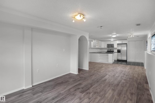 Open-concept living area with wood-finish flooring, recessed archway, and a kitchen featuring white cabinetry, black countertops, and stainless steel appliances - 907 Jordan Crescent Nw, Edmonton, AB - Indoor Photo Showing Kitchen