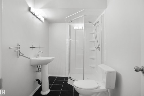 Pedestal sink, corner shower enclosure, black tile flooring, wall-mounted light fixture, and toilet - 907 Jordan Crescent Nw, Edmonton, AB - Indoor Photo Showing Bathroom