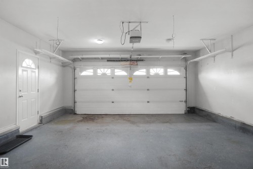 Attached single-car garage featuring a white paneled door with arched window inserts, a side entry door with a half-moon window, an automatic garage door opener, and overhead lighting - 907 Jordan Crescent Nw, Edmonton, AB - Indoor Photo Showing Garage