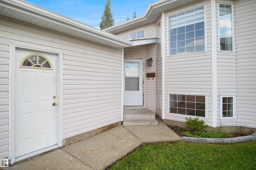 Exterior featuring light-colored siding, a prominent bay window, multiple window configurations, a concrete walkway, and a landscaped garden bed - 907 Jordan Crescent Nw, Edmonton, AB - Outdoor With Exterior