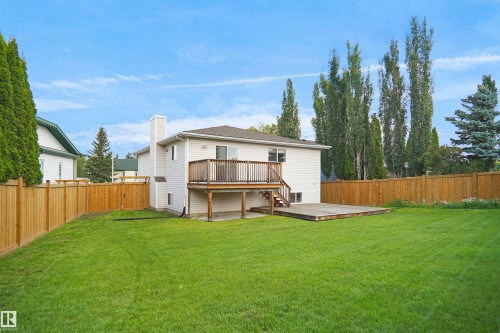 Expansive grassy yard with wood fencing, an elevated wood deck, and a ground-level wood patio - 907 Jordan Crescent Nw, Edmonton, AB - Outdoor With Backyard
