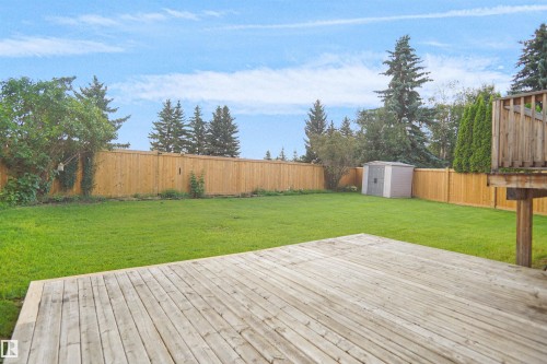Expansive lawn with a wood privacy fence, mature trees, an outdoor storage shed, and a raised wood deck - 907 Jordan Crescent Nw, Edmonton, AB - Outdoor With Deck Patio Veranda With Backyard