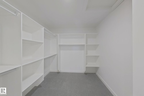 Spacious walk-in closet featuring built-in shelving, hanging rods, and light gray carpeting - 3158 Magpie Way Nw, Edmonton, AB - Indoor With Storage