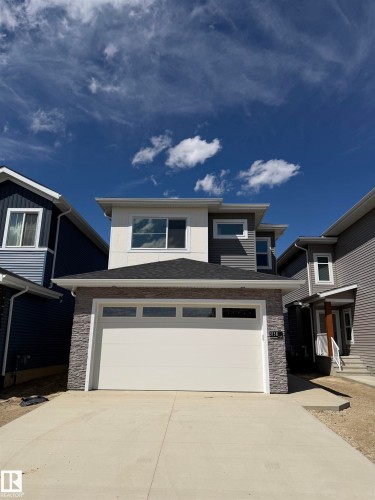 Multi-level contemporary exterior with horizontal siding, stone facade accents, a sloped roofline, and an attached garage with translucent paneling - 3158 Magpie Way Nw, Edmonton, AB - Outdoor With Facade