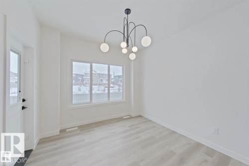 Laminate wood-finish flooring, contemporary chandelier, large picture window, and white interior walls - 3158 Magpie Way Nw, Edmonton, AB - Indoor Photo Showing Other Room