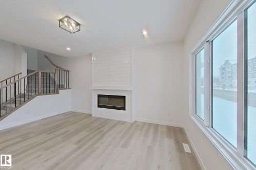 Contemporary linear fireplace with shiplap-style surround, wood-finish flooring, and a modern stair railing with black spindles - 3158 Magpie Way Nw, Edmonton, AB - Indoor With Fireplace