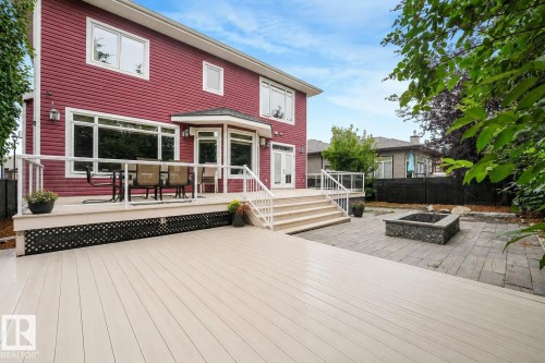 Expansive multi-level deck, red siding exterior with white trim windows, double French patio doors, paver stone patio, and a built-in stone fire pit - 27 Kingdom Place, Leduc, AB - Outdoor With Deck Patio Veranda