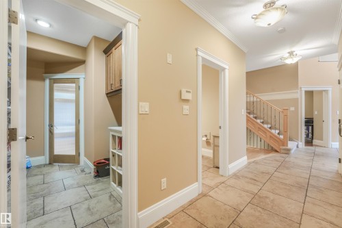 Hallway featuring large format tile flooring, crown molding, a built-in storage unit, and a staircase with wood newel posts and wrought iron balusters - 27 Kingdom Place, Leduc, AB - Indoor Photo Showing Other Room