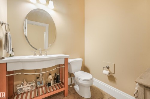 Oval wall mirror, chrome faucet, white integrated sink, wood-finish vanity with open shelving, and tile flooring - 27 Kingdom Place, Leduc, AB - Indoor Photo Showing Bathroom