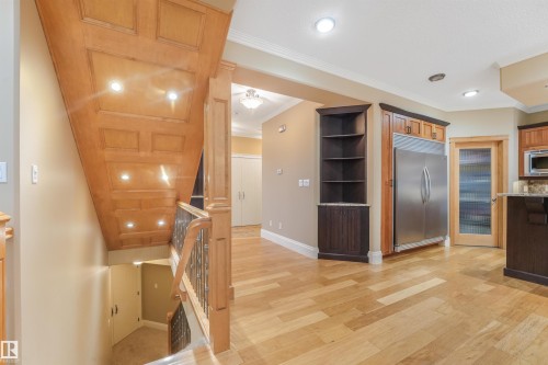 Wood-finish flooring, paneled wood staircase with recessed lighting, wrought iron stair railing, built-in shelving, and stainless steel refrigerator - 27 Kingdom Place, Leduc, AB - Indoor Photo Showing Kitchen