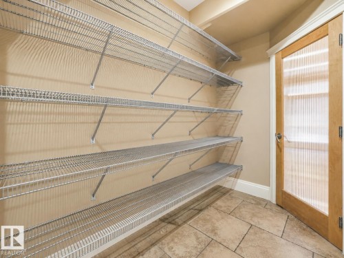 Wall-mounted wire shelving system, light-toned wall finish, tile flooring, wood-frame door with textured glass panel, and white trim - 27 Kingdom Place, Leduc, AB - Indoor With Storage