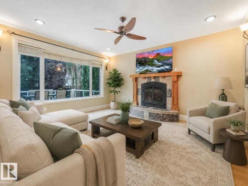 Expansive windows, ceiling-mounted fan, recessed lighting, stone-surround fireplace with wood mantel, and light wall tones - 27 Kingdom Place, Leduc, AB - Indoor Photo Showing Living Room With Fireplace