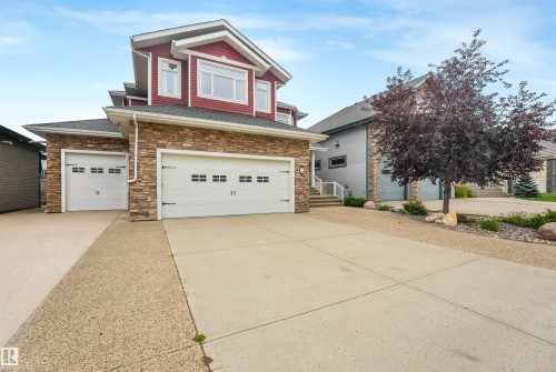 Stone facade with red siding, multi-car garage, and concrete driveway - 27 Kingdom Place, Leduc, AB - Outdoor With Facade