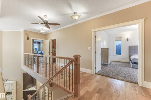 Wood-finish flooring, staircase with wood railing and wrought iron balusters, ceiling fans with integrated lighting, recessed lighting, and wall sconces - 27 Kingdom Place, Leduc, AB - Indoor Photo Showing Other Room