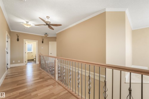 Wood-finish flooring, ceiling fan, crown molding, and a staircase with wrought iron balusters - 27 Kingdom Place, Leduc, AB - Indoor Photo Showing Other Room