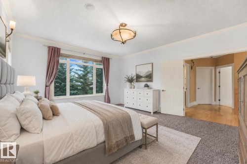 Large window with exterior foliage, wall sconces, ceiling-mounted light fixture, white interior doors, and wood-finish flooring - 27 Kingdom Place, Leduc, AB - Indoor Photo Showing Bedroom