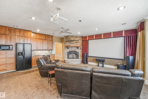 Expansive recreation room featuring a wood-finish plank floor, stone fireplace with hearth, and a professional-grade projection screen with red velvet drapery - 27 Kingdom Place, Leduc, AB - Indoor With Fireplace