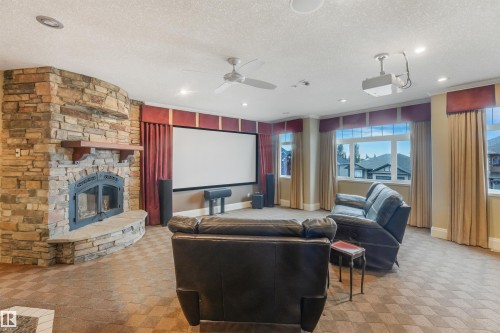 Built-in stone fireplace with a wood mantle, ceiling-mounted projector, large projection screen, multiple windows, and recessed lighting - 27 Kingdom Place, Leduc, AB - Indoor Photo Showing Living Room With Fireplace