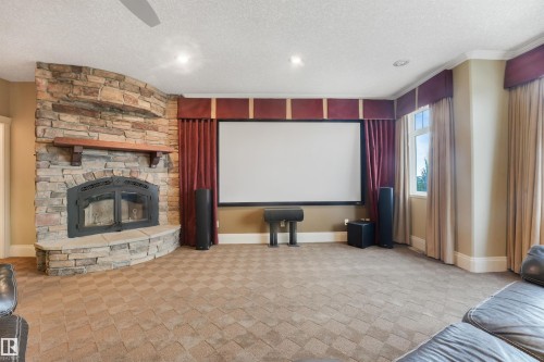 Stone-clad fireplace with a wood mantel, large projection screen, recessed lighting, patterned carpeting, and crown molding - 27 Kingdom Place, Leduc, AB - Indoor With Fireplace